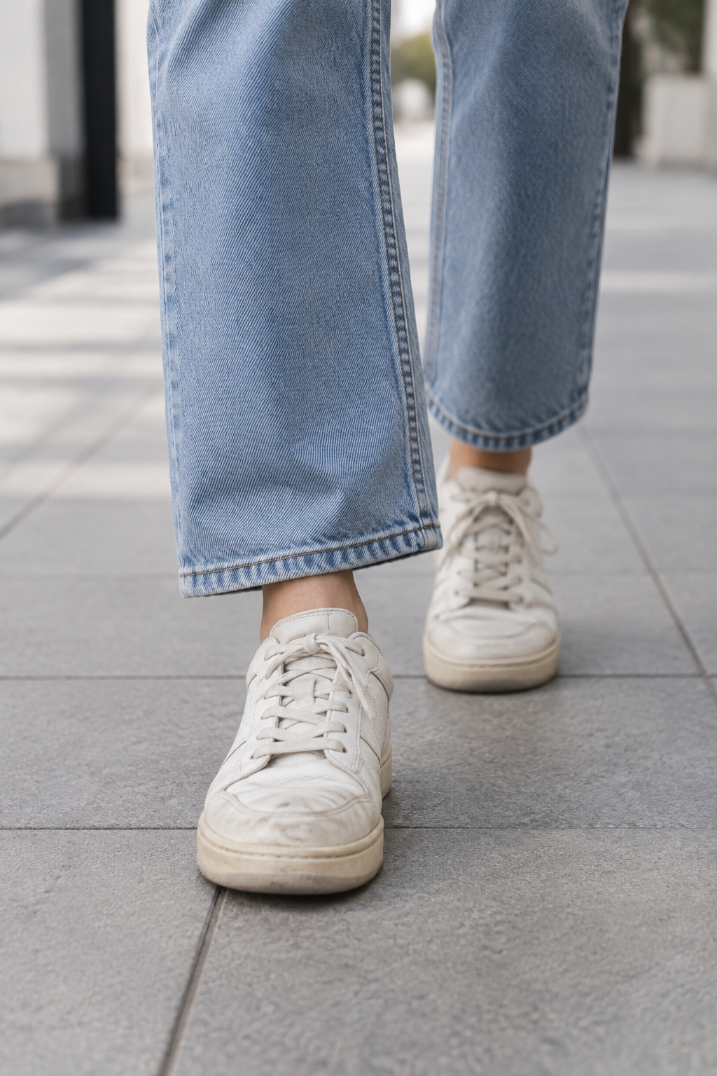 Pies con tenis blancos gastados caminando por un andén